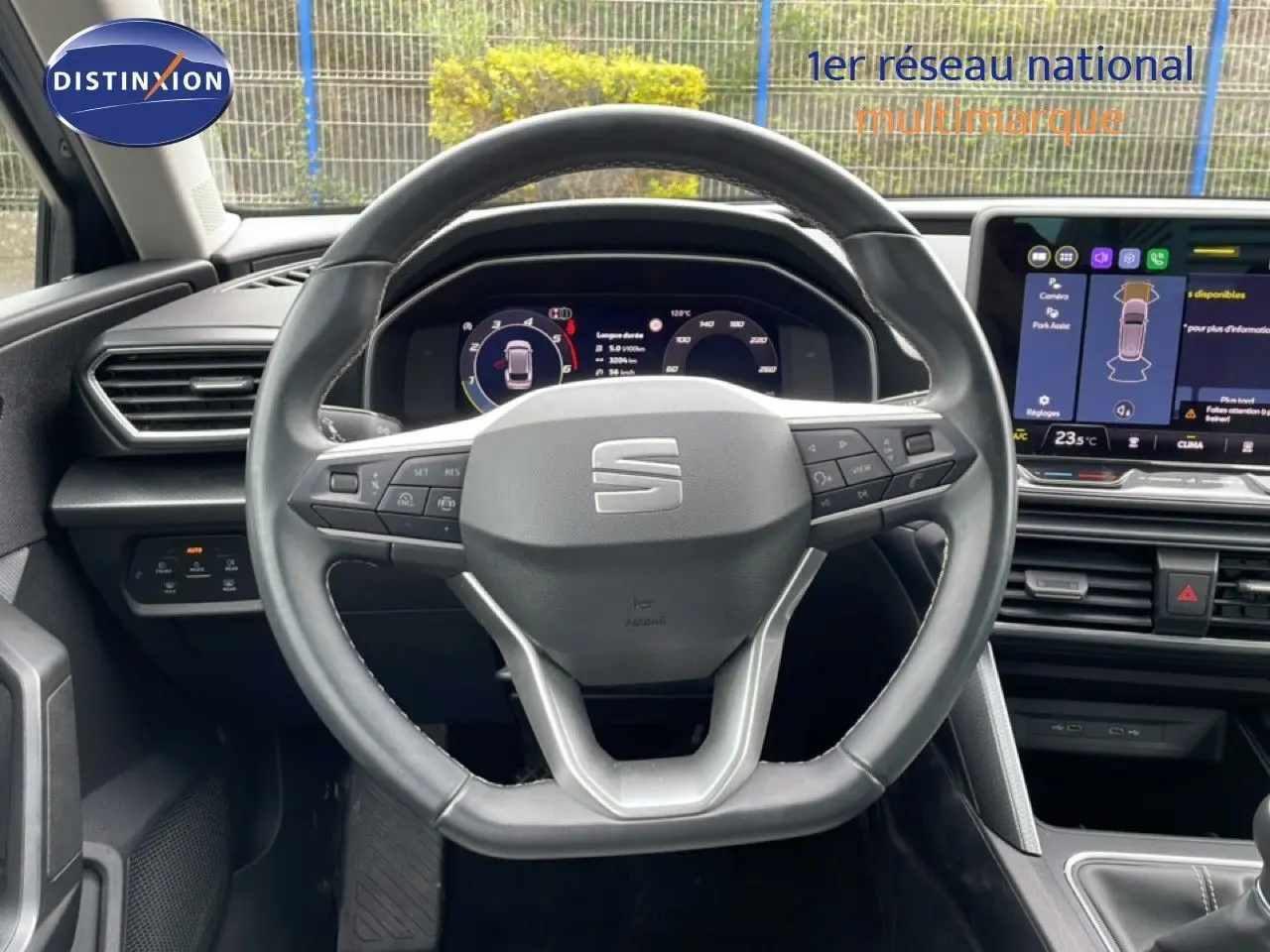 Vue intérieure centrée sur le volant cuir multifonction d'une SEAT LEON ST 2025, avec tableau de bord digital et écran tactile.