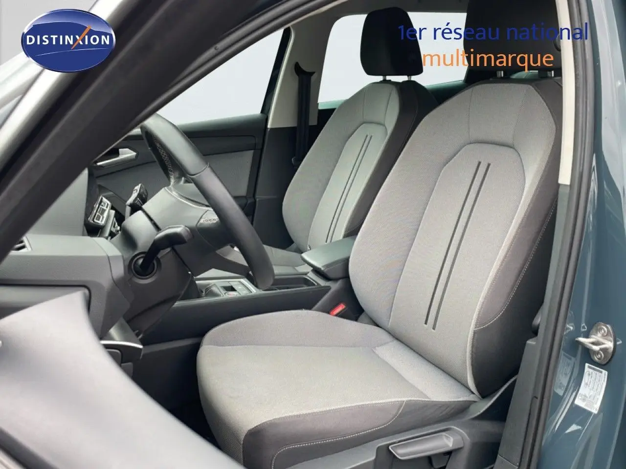 Vue intérieure côté conducteur du SEAT LEON ST gris métallique, montrant les sièges tissu gris clair et le volant multifonction.