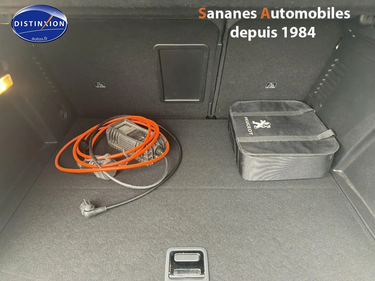 Coffre ouvert d’un Peugeot 3008 Hybrid blanc, vue plongeante montrant câble de recharge et sacoche Peugeot.