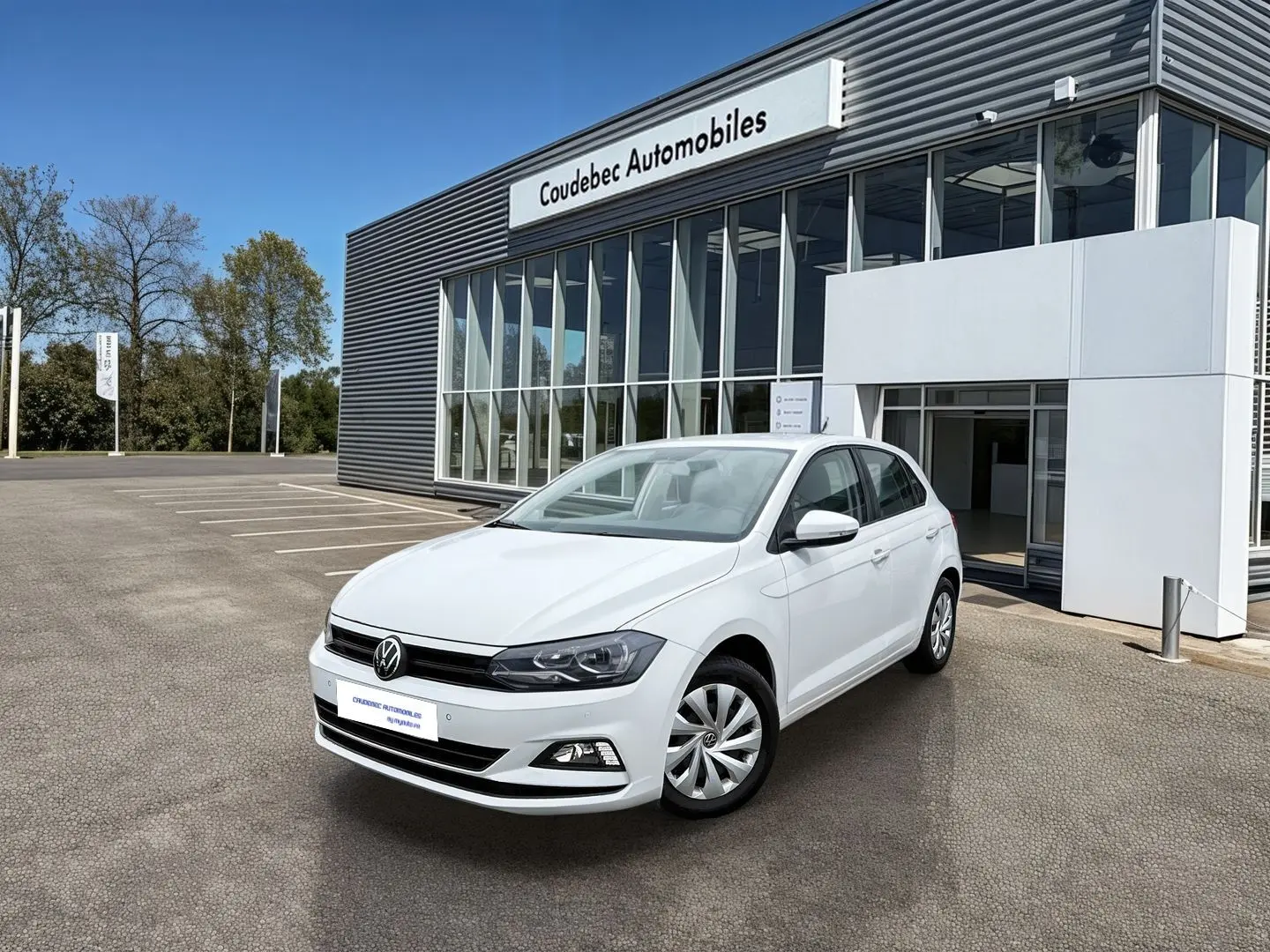 Volkswagen Polo Business blanche vue en 3/4 avant droit devant un bâtiment de concession automobile.