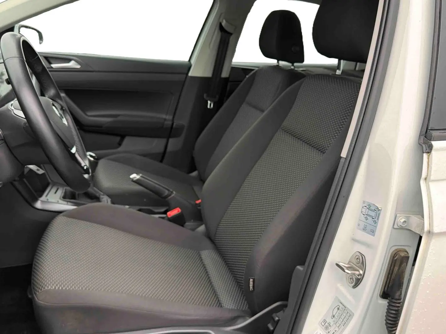 Vue intérieure côté gauche de la Volkswagen Polo Business 2021 blanche, montrant les sièges avant en tissu gris et le volant.