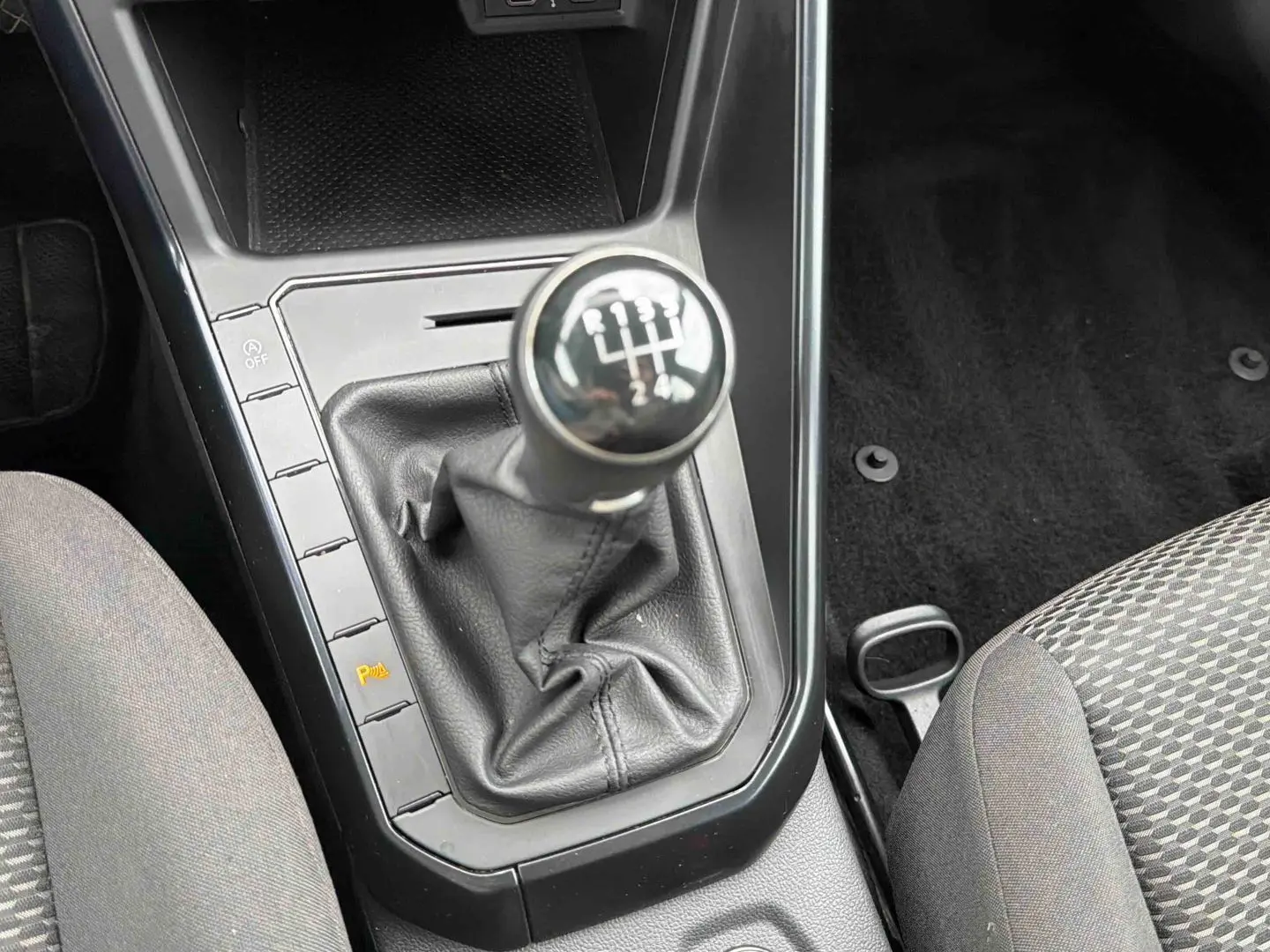 Gros plan sur le levier de vitesses manuel noir de la Volkswagen Polo Business 2021, entouré de sièges gris à motifs.