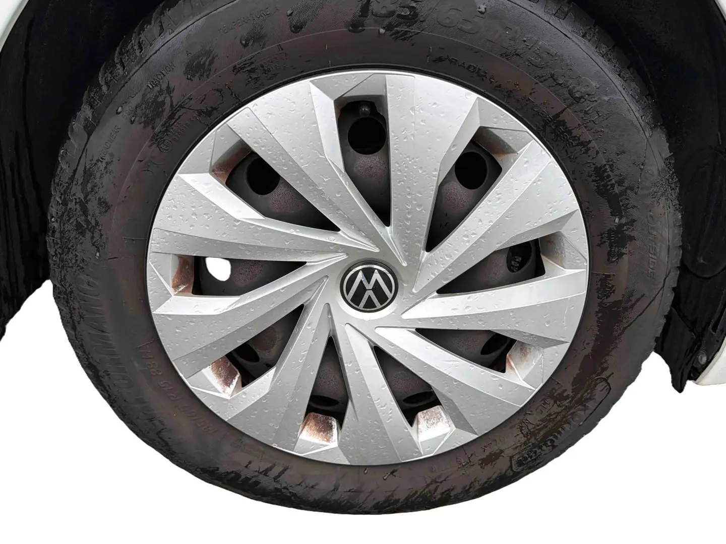 Gros plan sur la roue avant droite d’une Volkswagen Polo Business blanche avec enjoliveur argenté et traces d’humidité.