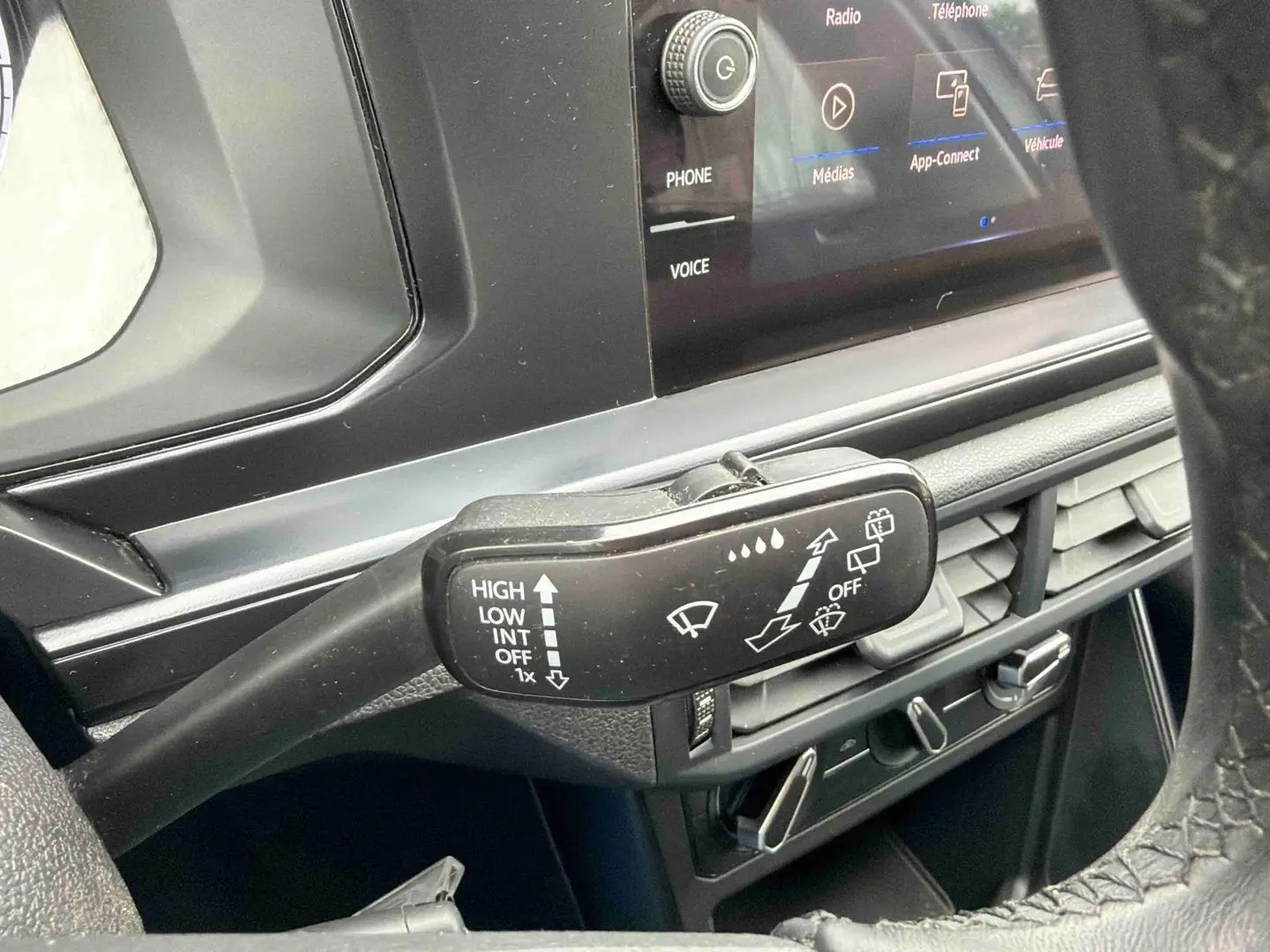 Gros plan sur la commande d’essuie-glace côté gauche du tableau de bord noir d’une Volkswagen Polo blanche.