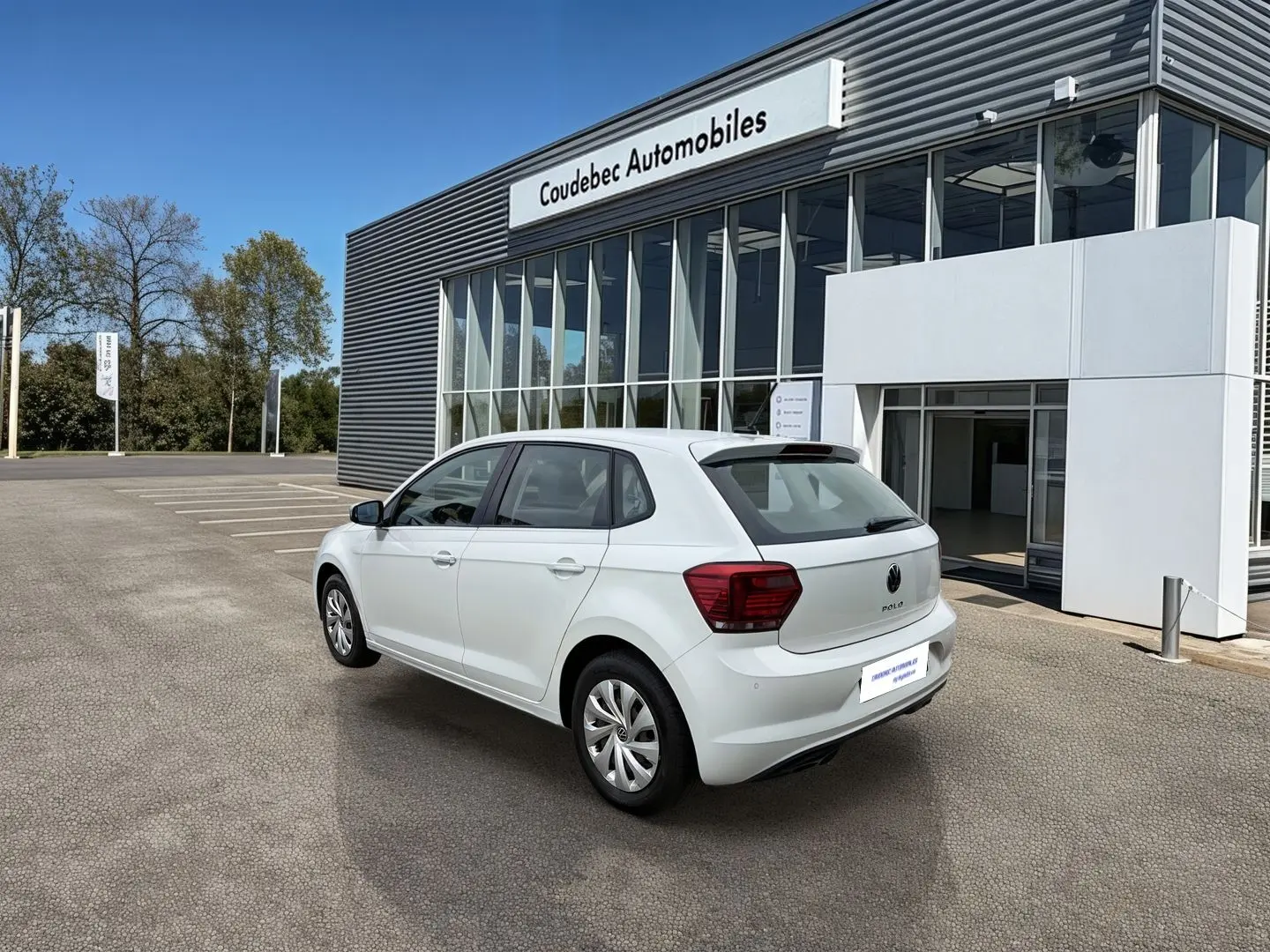 Volkswagen Polo Business blanche vue 3/4 arrière droit, avec jantes acier et feux arrière rouges, devant un garage.