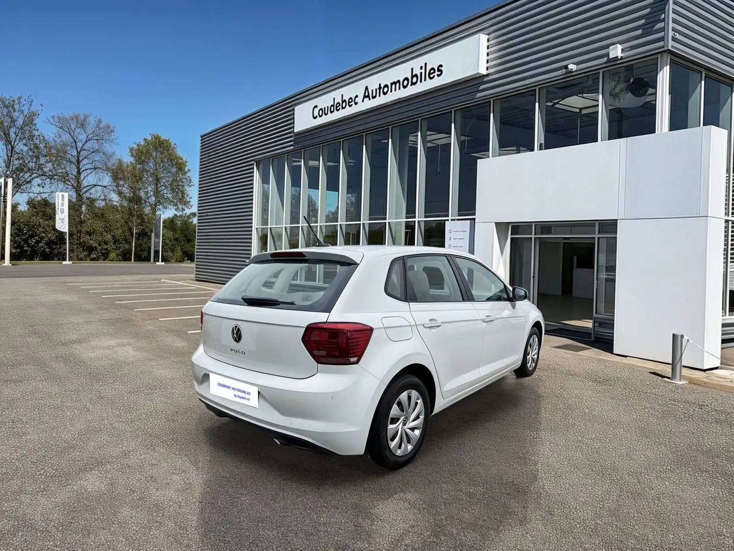 Volkswagen Polo Business blanche vue 3/4 arrière droit devant un bâtiment commercial.