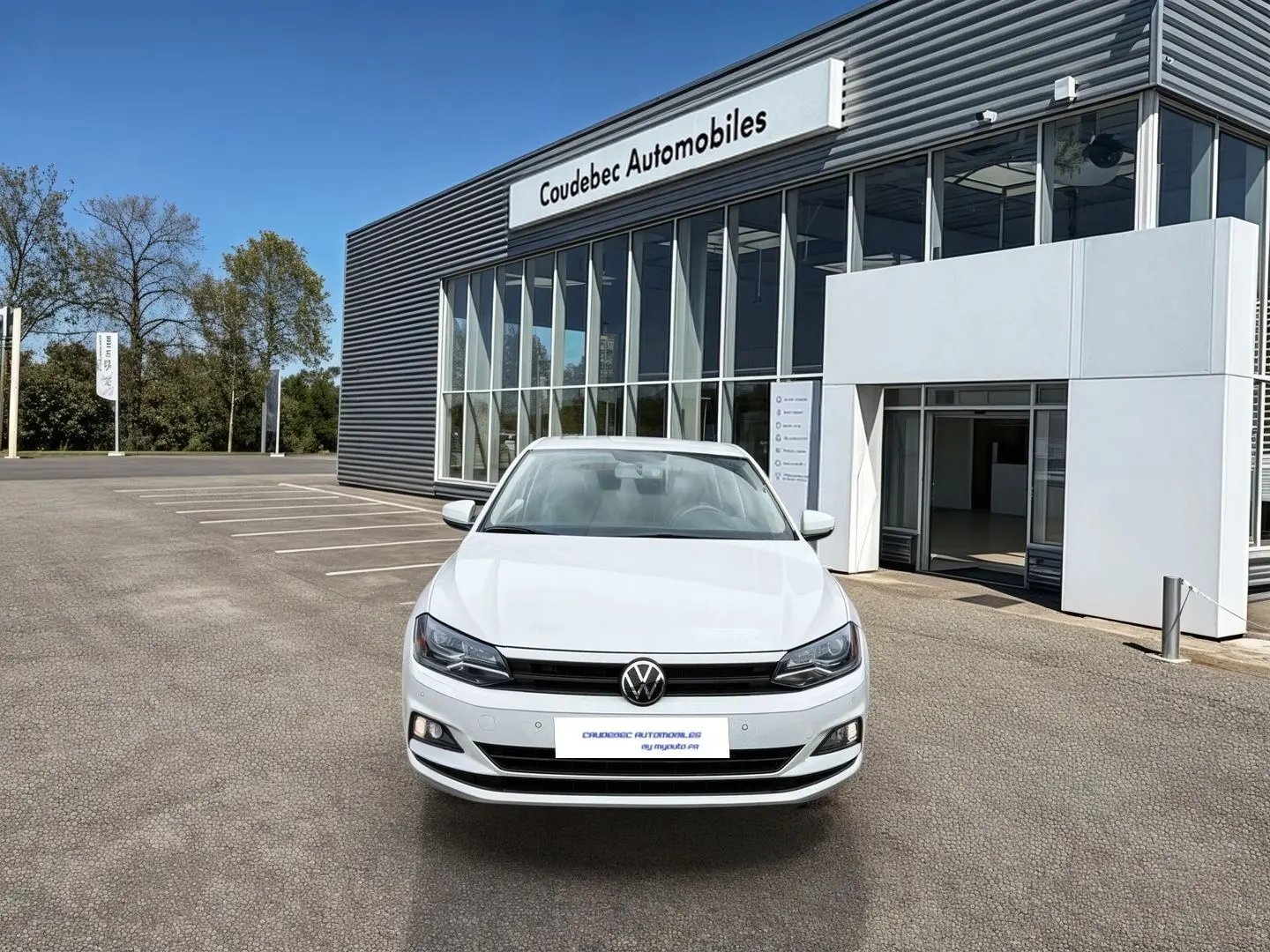 Volkswagen Polo Business blanche vue de face, stationnée devant un bâtiment commercial moderne.