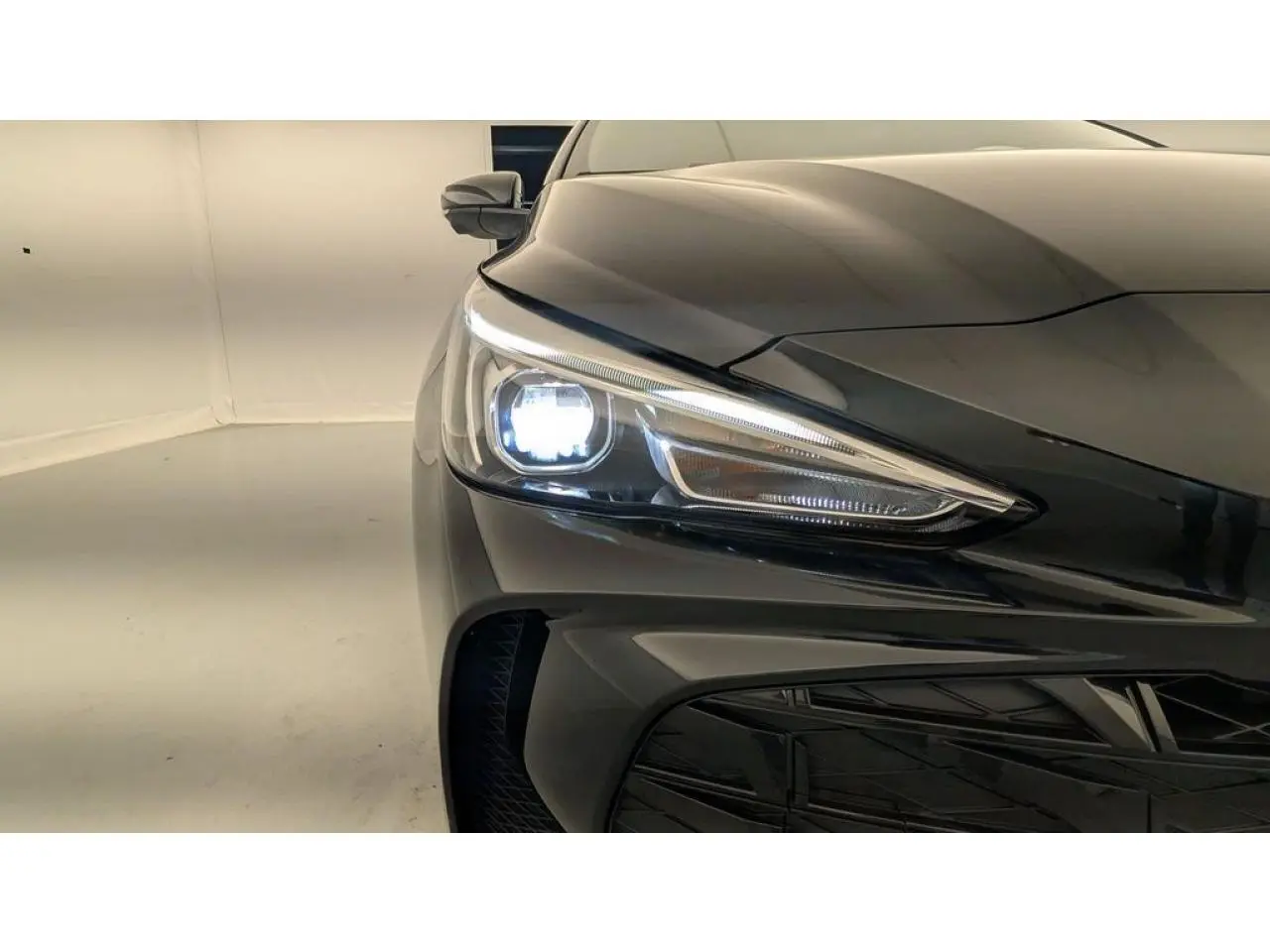 Gros plan sur l'avant droit noir métallisé du MG3 1.5 Hybrid+ 195 Luxury avec phare allumé et calandre visible.