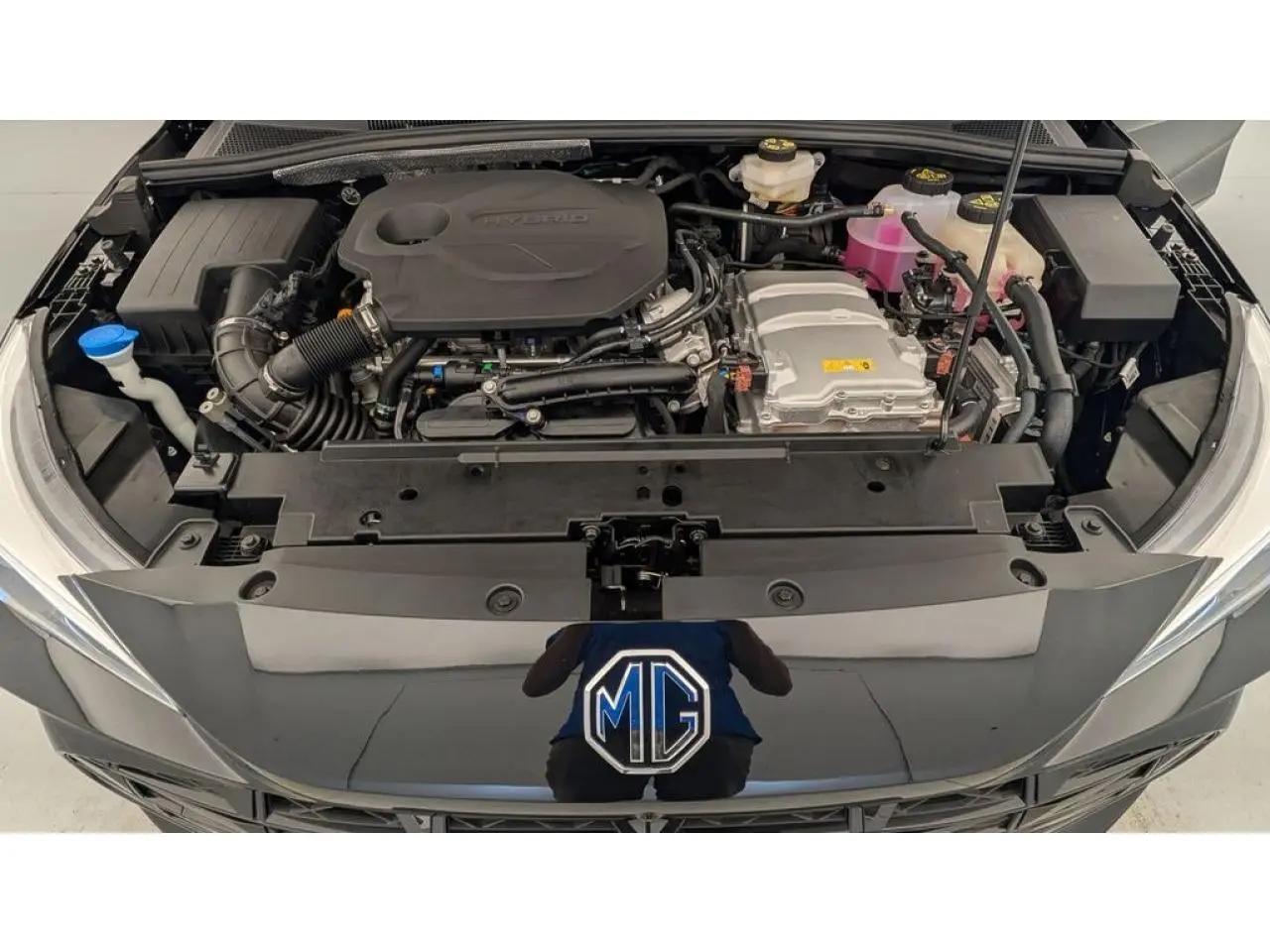 Vue plongeante sur le moteur hybride d'une MG3 1.5 Hybrid+ noire, capot ouvert avec logo MG visible.