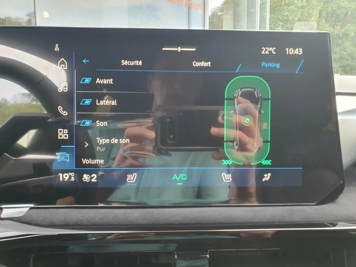 Écran tactile intérieur de la Renault Clio VI affichant les réglages de sécurité et parking, avec reflet du conducteur.