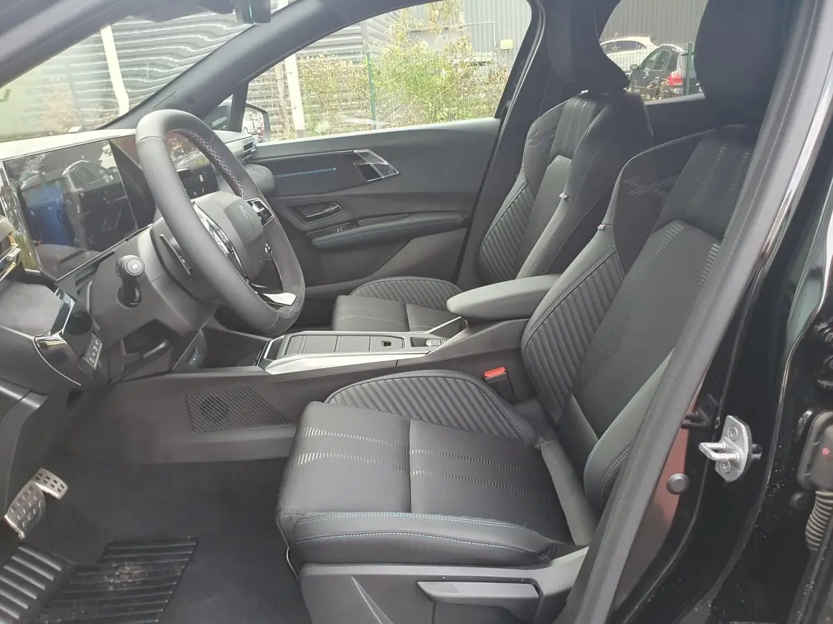 Intérieur de la Renault Clio VI noire étoile, vue côté gauche, sièges avant en tissu avec surpiqûres bleues.