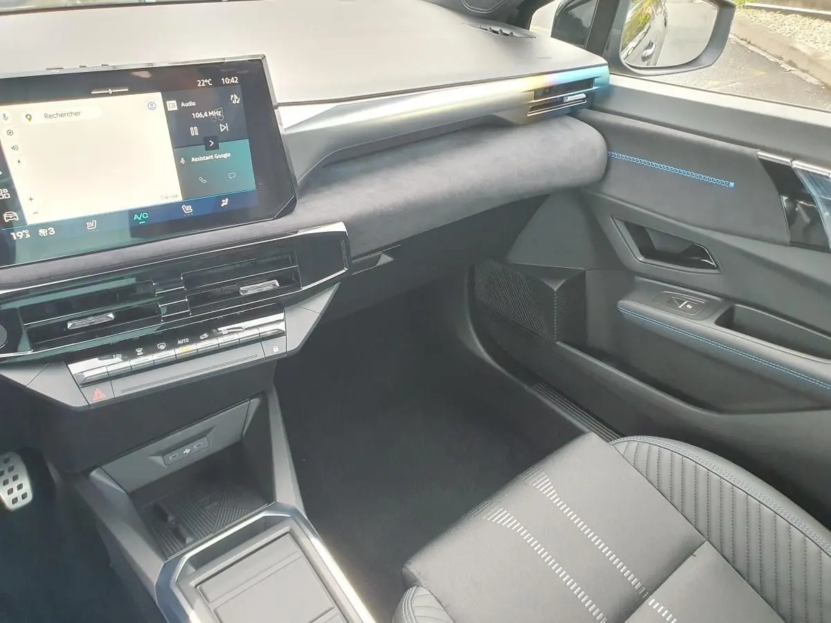 Intérieur avant droit de la Renault Clio VI noire étoile, avec écran tactile et surpiqûres bleues sur la portière.