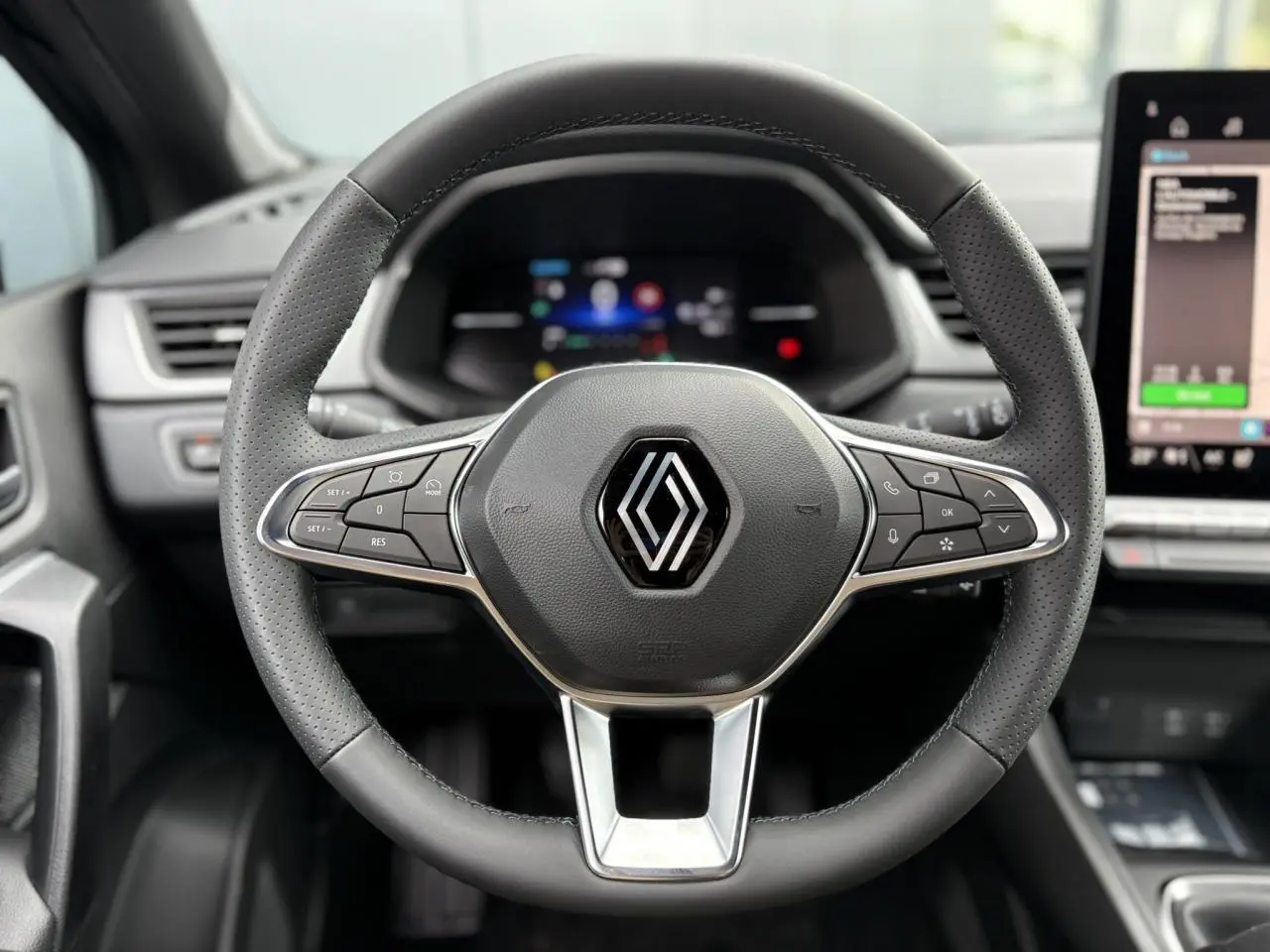 Volant en cuir noir perforé de Renault Captur 2025 avec commandes intégrées et tableau de bord numérique flou en arrière-plan.