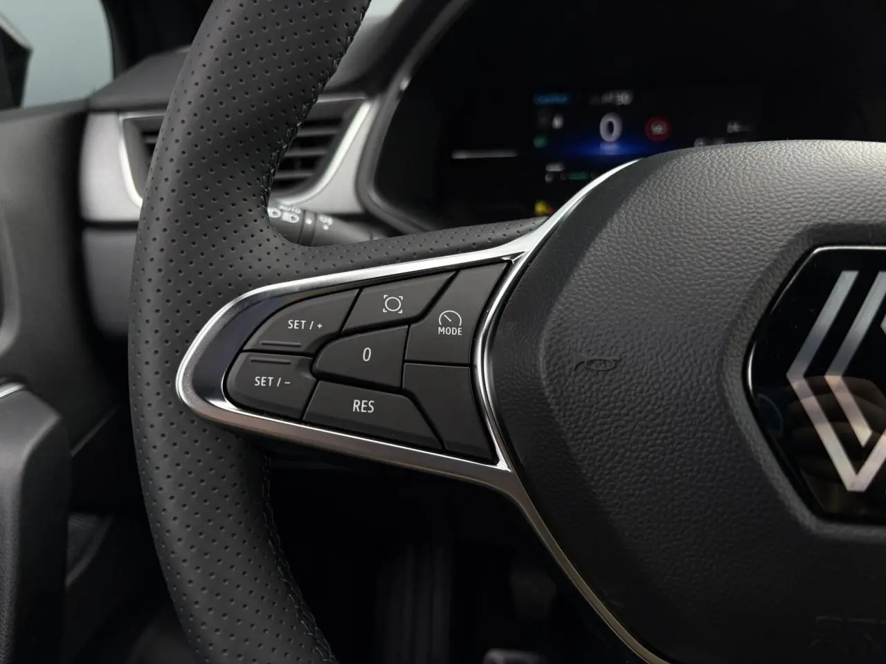 Gros plan sur le volant perforé du Renault Captur Noir Étoile 2025 avec commandes intégrées et logo central visible.