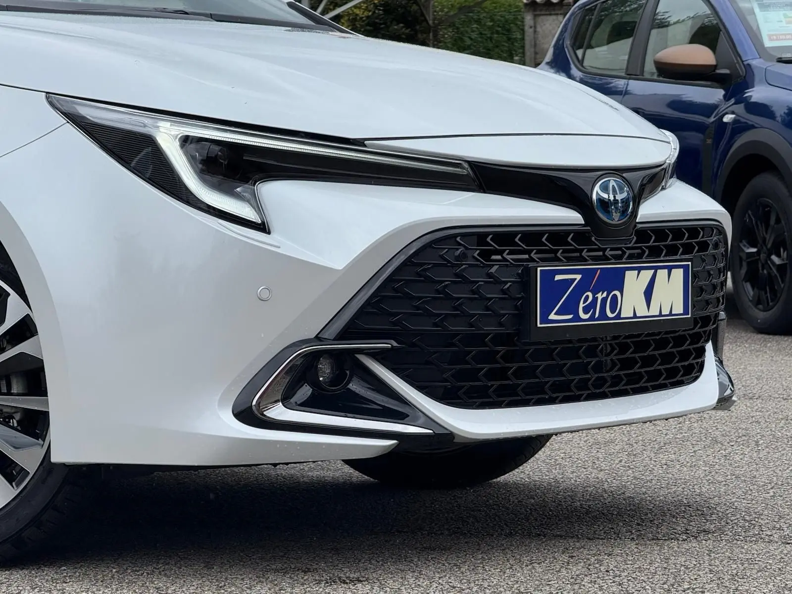 Gros plan sur l'avant droit blanc lunaire nacré de la Toyota Corolla Touring Sport 2025 avec calandre noire et phares LED.