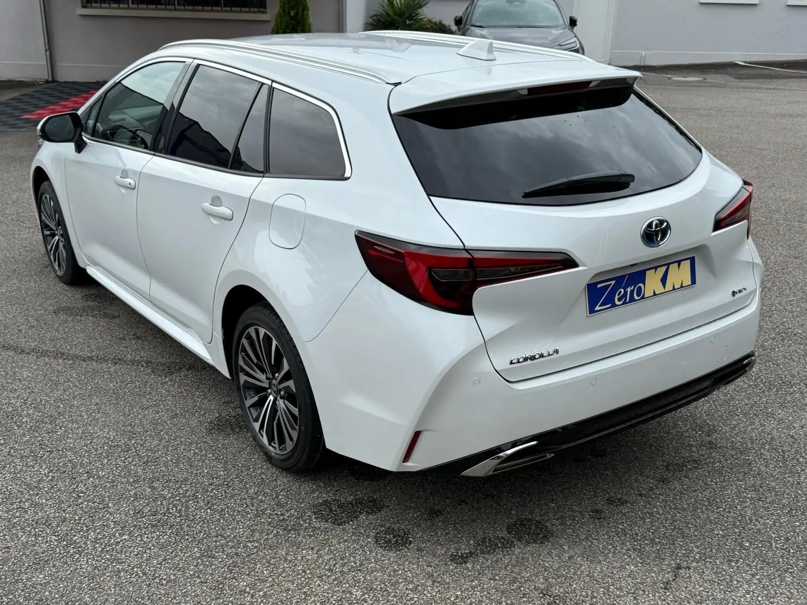 Toyota Corolla Touring Sport blanc lunaire nacré vue 3/4 arrière droit avec vitres teintées et jantes alliage noires.