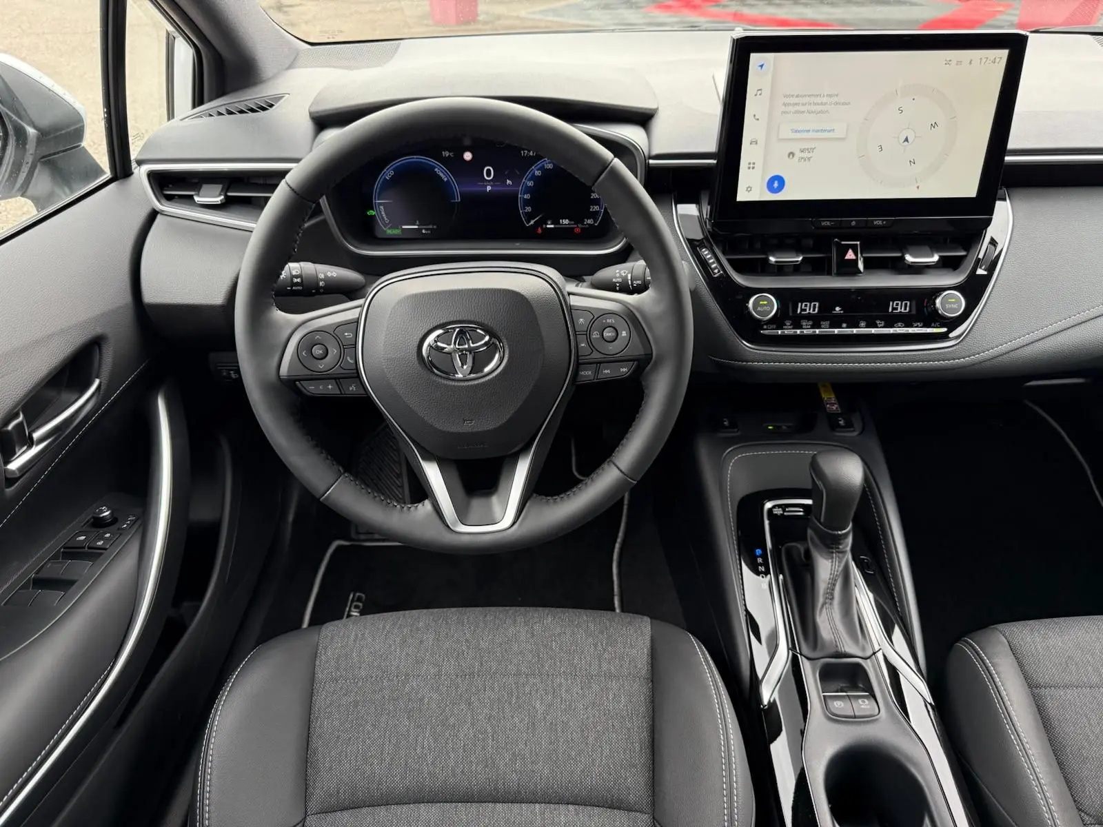 Vue intérieure frontale du poste de conduite de la Toyota Corolla Touring Sport 2025, avec volant multifonction et écran tactile central.
