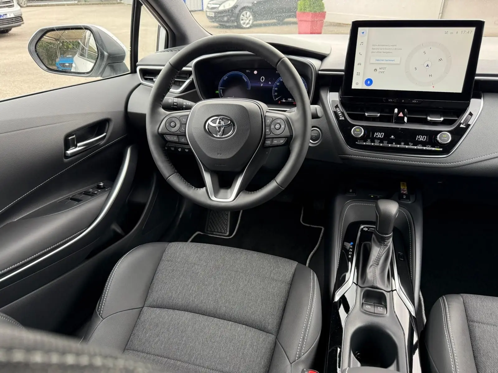 Vue intérieure avant centrée sur le volant et la console centrale d'une Toyota Corolla Touring Sport 2025, finition Active Plus.