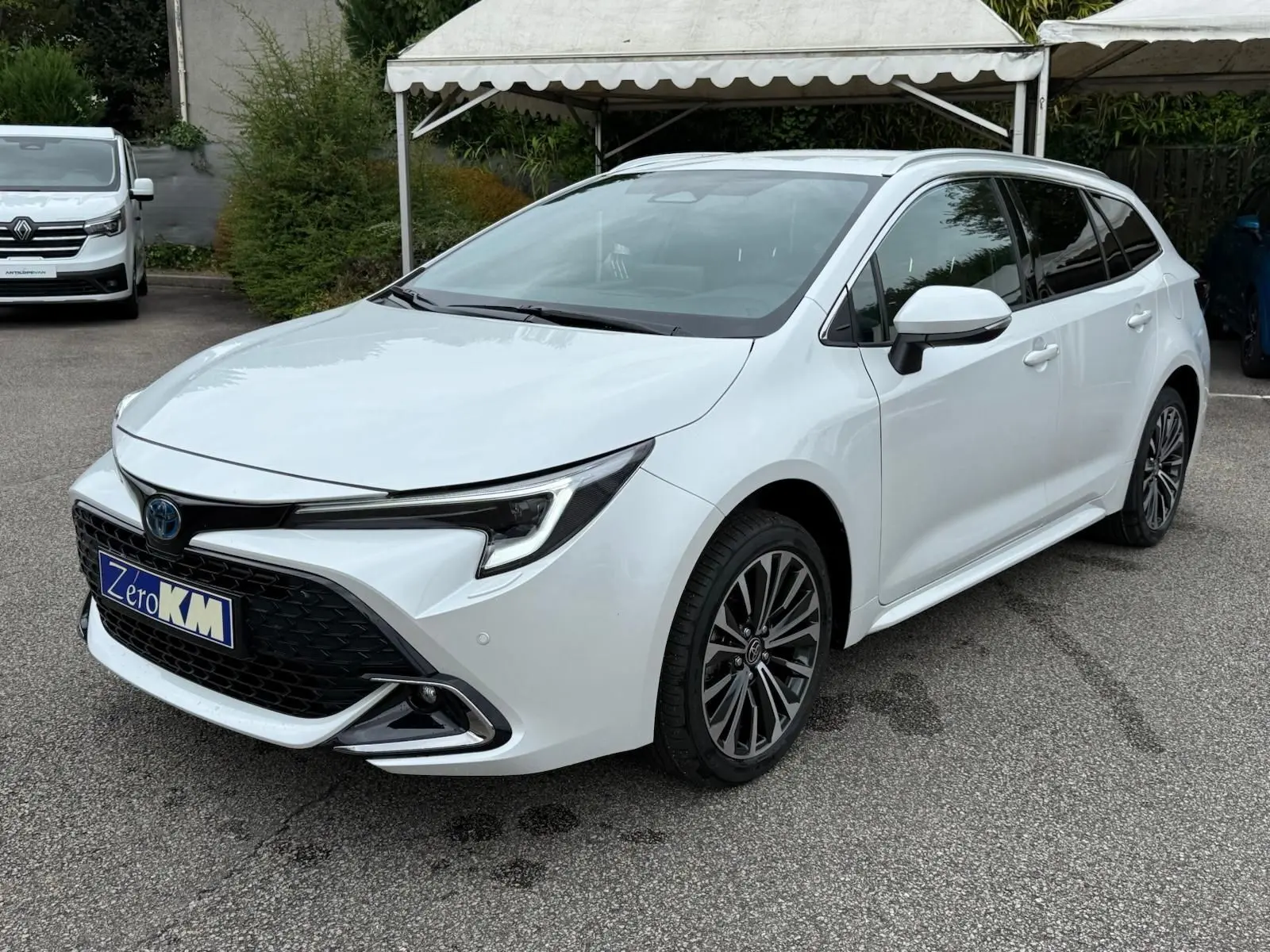 Toyota Corolla Touring Sport blanc lunaire nacré en 3/4 avant droit avec calandre noire et jantes alliage multibranches.