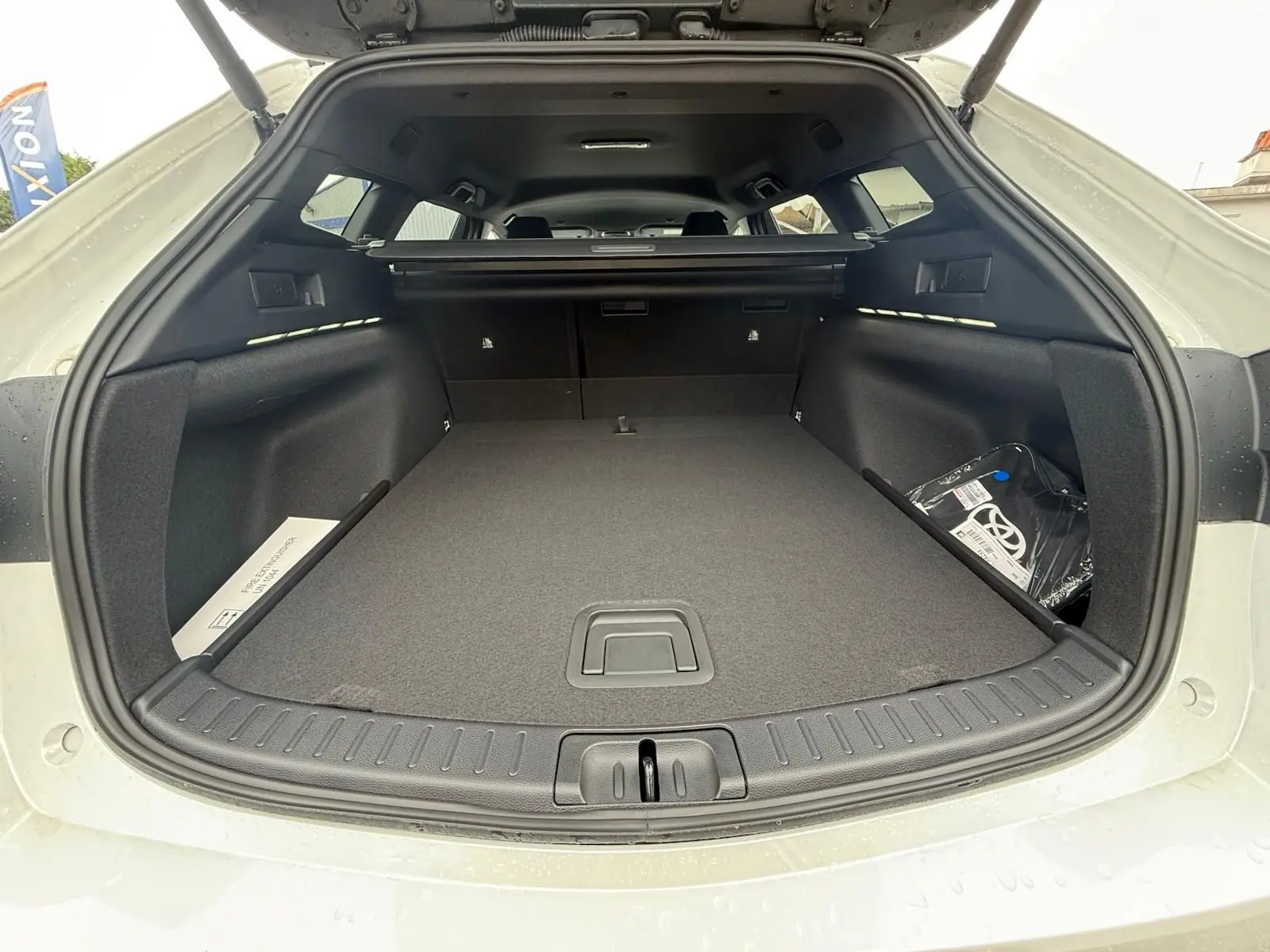 Coffre ouvert vu de l'arrière d'une Toyota Corolla Touring Sport blanche nacrée, montrant un espace de chargement spacieux et propre.