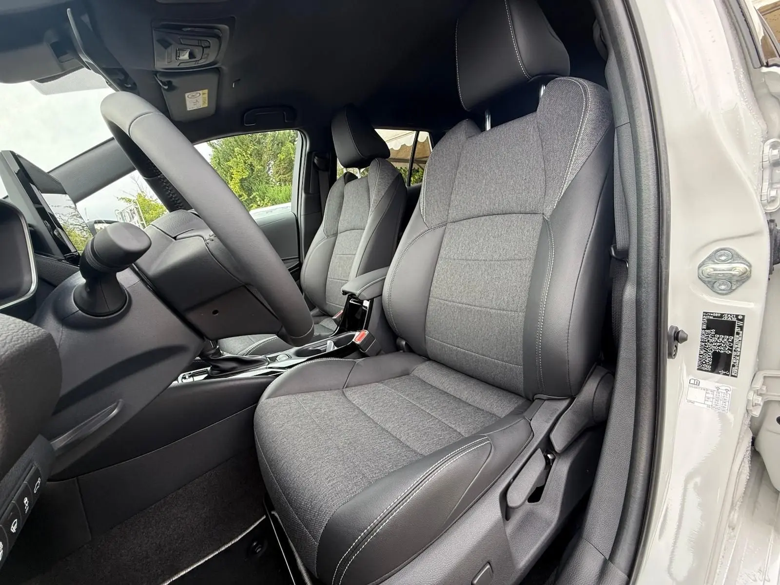 Intérieur côté conducteur de la Toyota Corolla Touring Sport blanche, sièges tissu gris et cuir noir avec surpiqûres blanches.