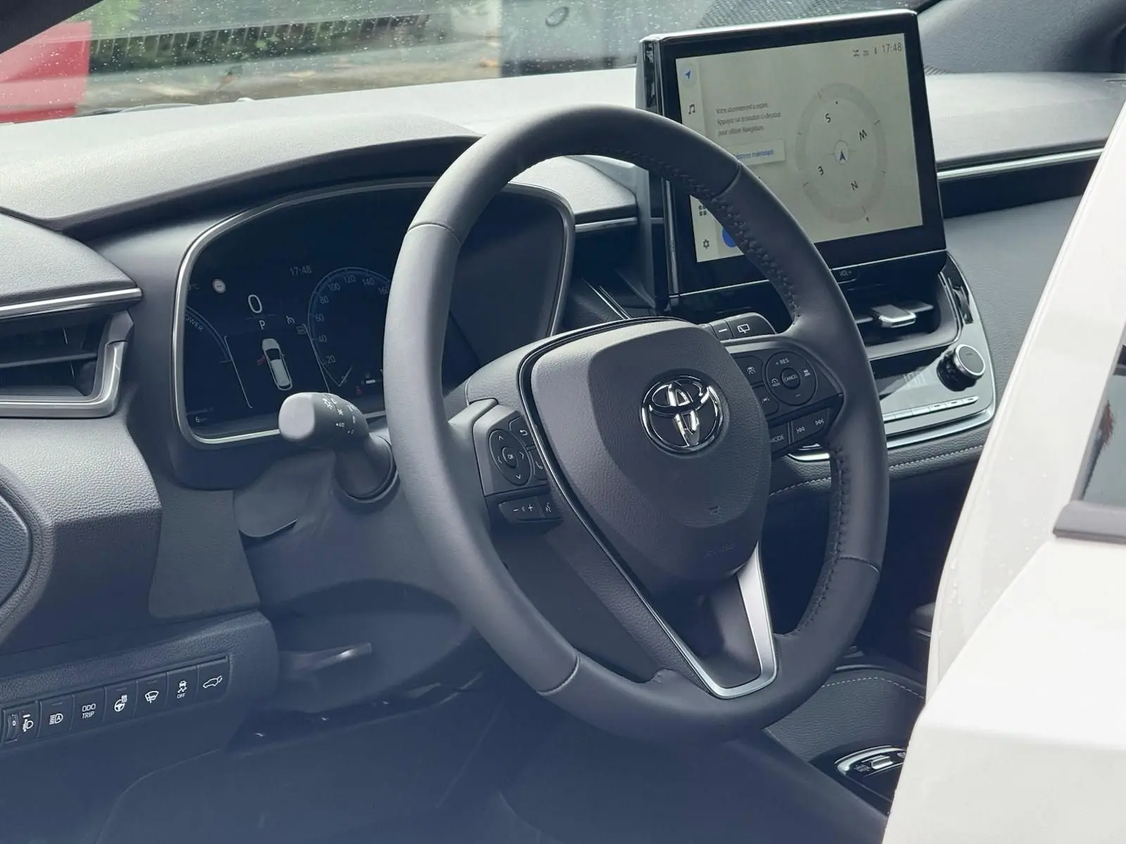 Vue intérieure côté conducteur de la Toyota Corolla Touring Sport blanche, avec volant multifonction et écran tactile central.
