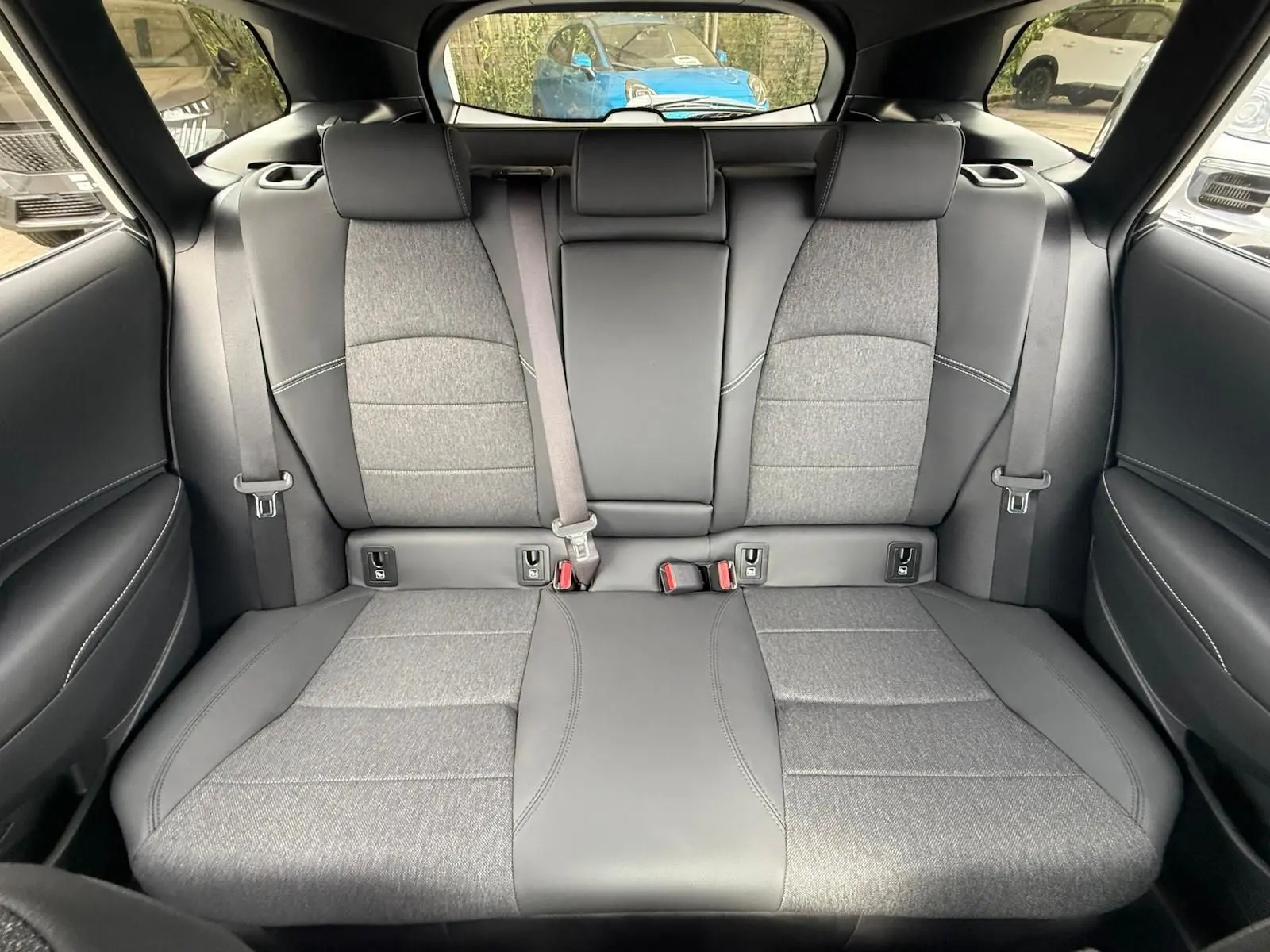 Banquette arrière en tissu gris et cuir noir de la Toyota Corolla Touring Sport 2025 vue de face, avec ceintures et appuie-têtes.