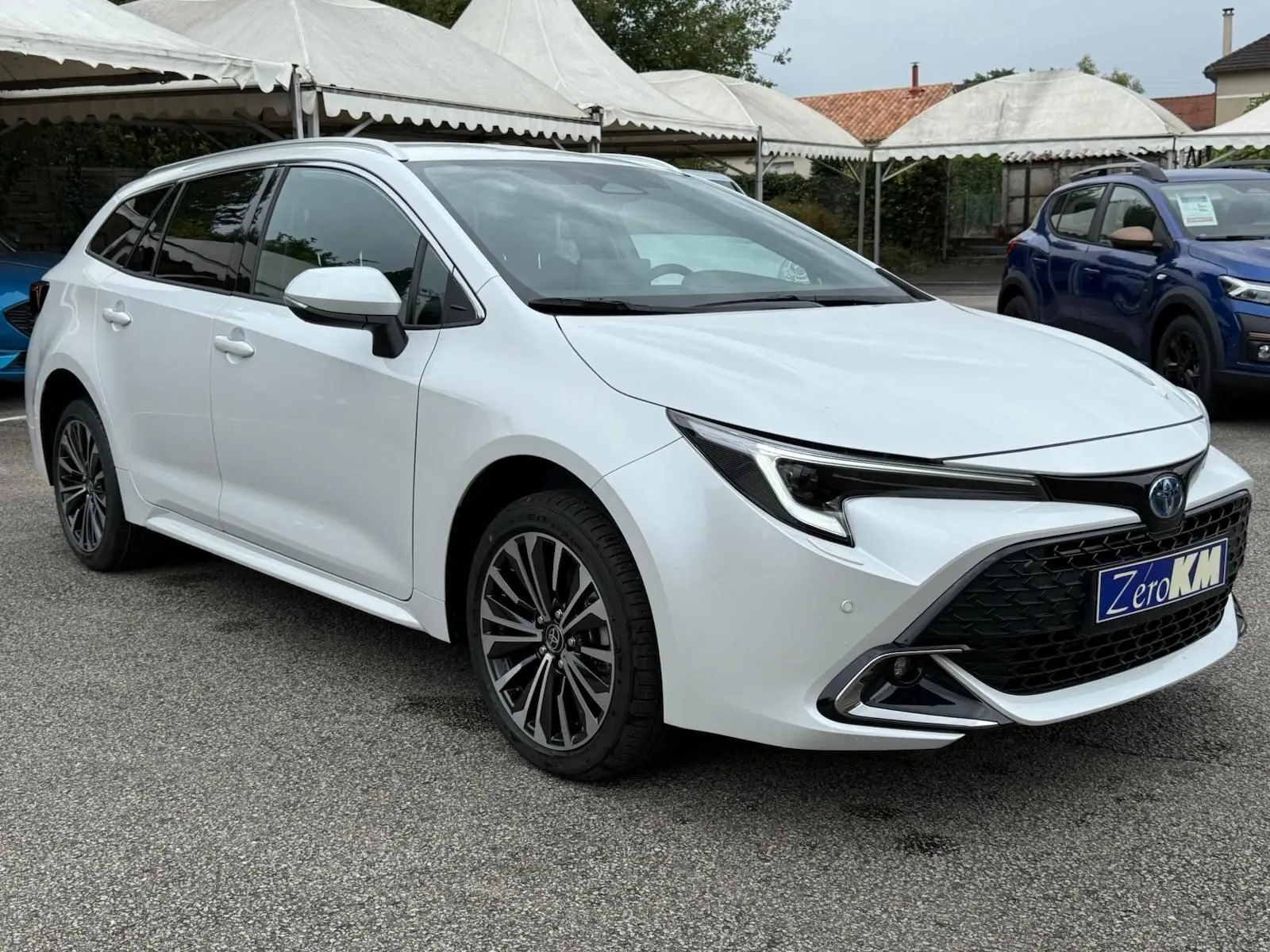 Toyota Corolla Touring Sport blanche nacrée vue en 3/4 avant droit, avec calandre noire et jantes alliage distinctives.