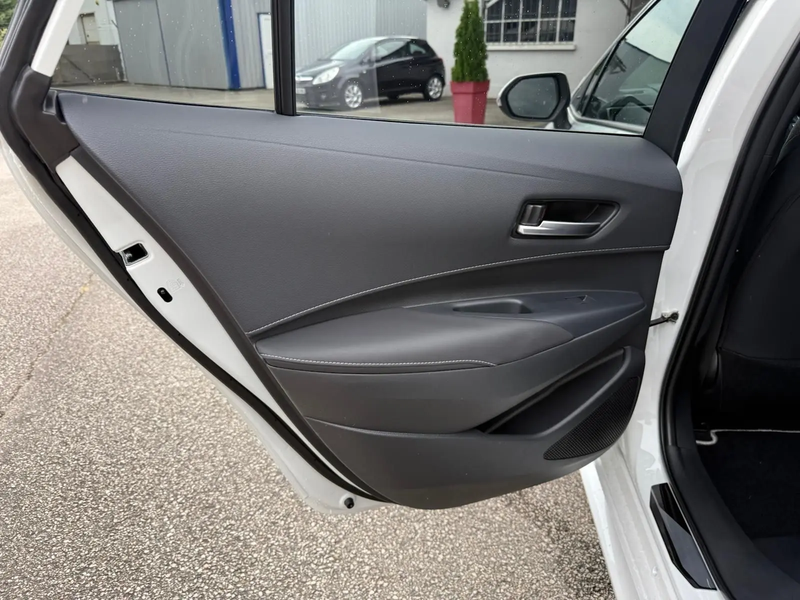 Vue rapprochée de la porte arrière droite noire avec surpiqûres blanches de la Toyota Corolla Touring Sport blanche lunaire nacrée.