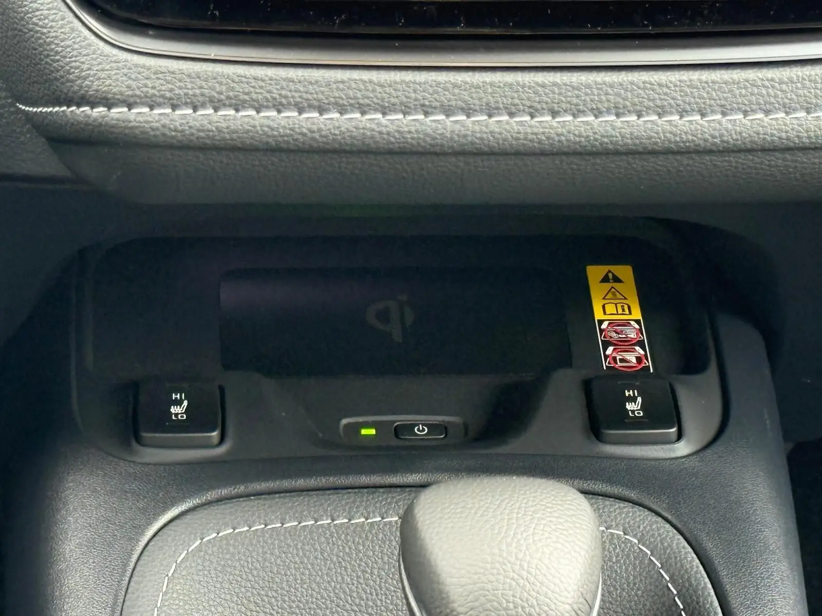 Gros plan sur la console centrale de la Toyota Corolla Touring Sport blanche, montrant les commandes de sièges chauffants et un chargeur sans fil.