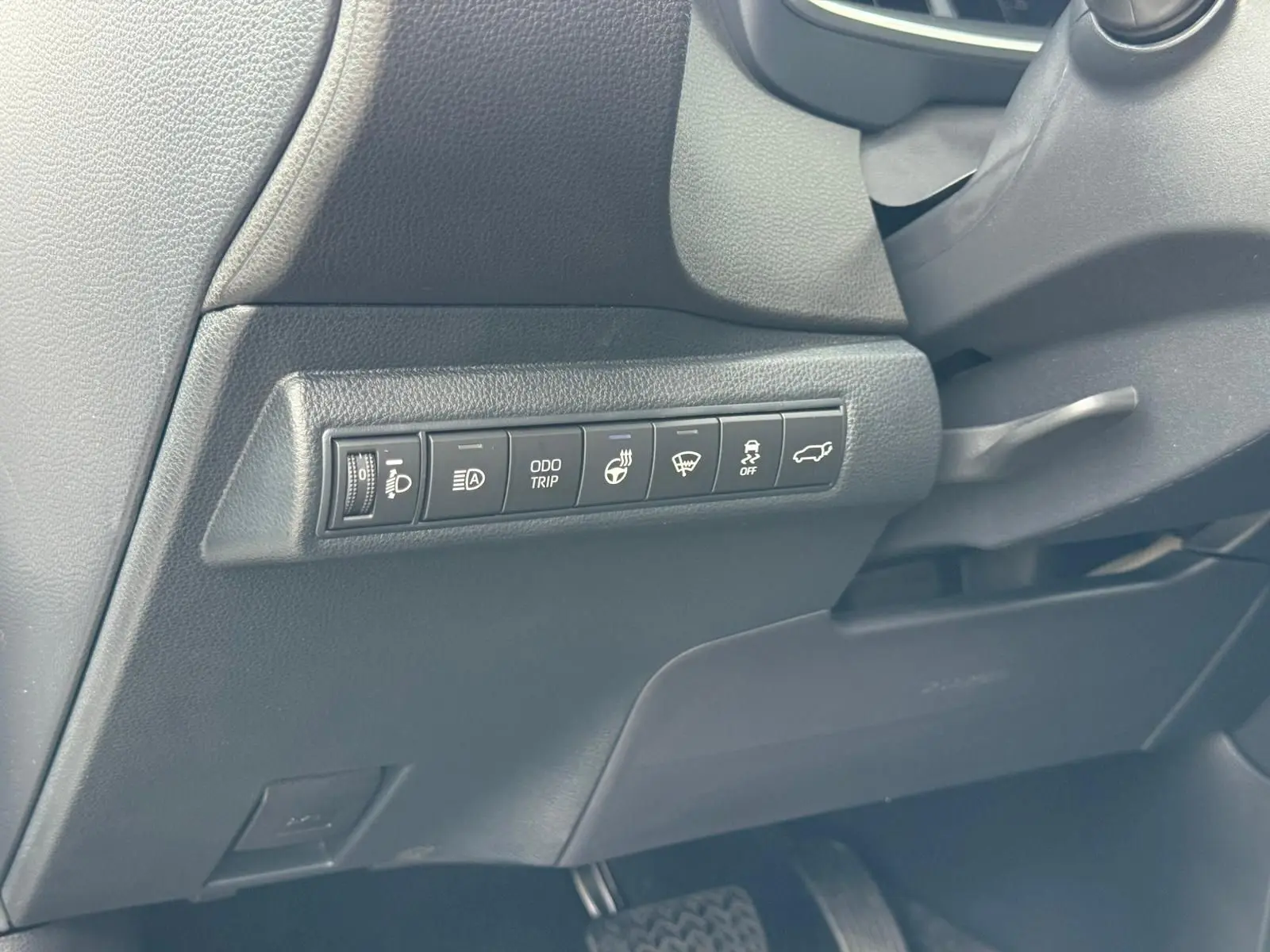 Panneau de commandes latéral noir avec boutons de réglages et fonctions sur le côté gauche du tableau de bord Toyota Corolla Touring Sport 2025.