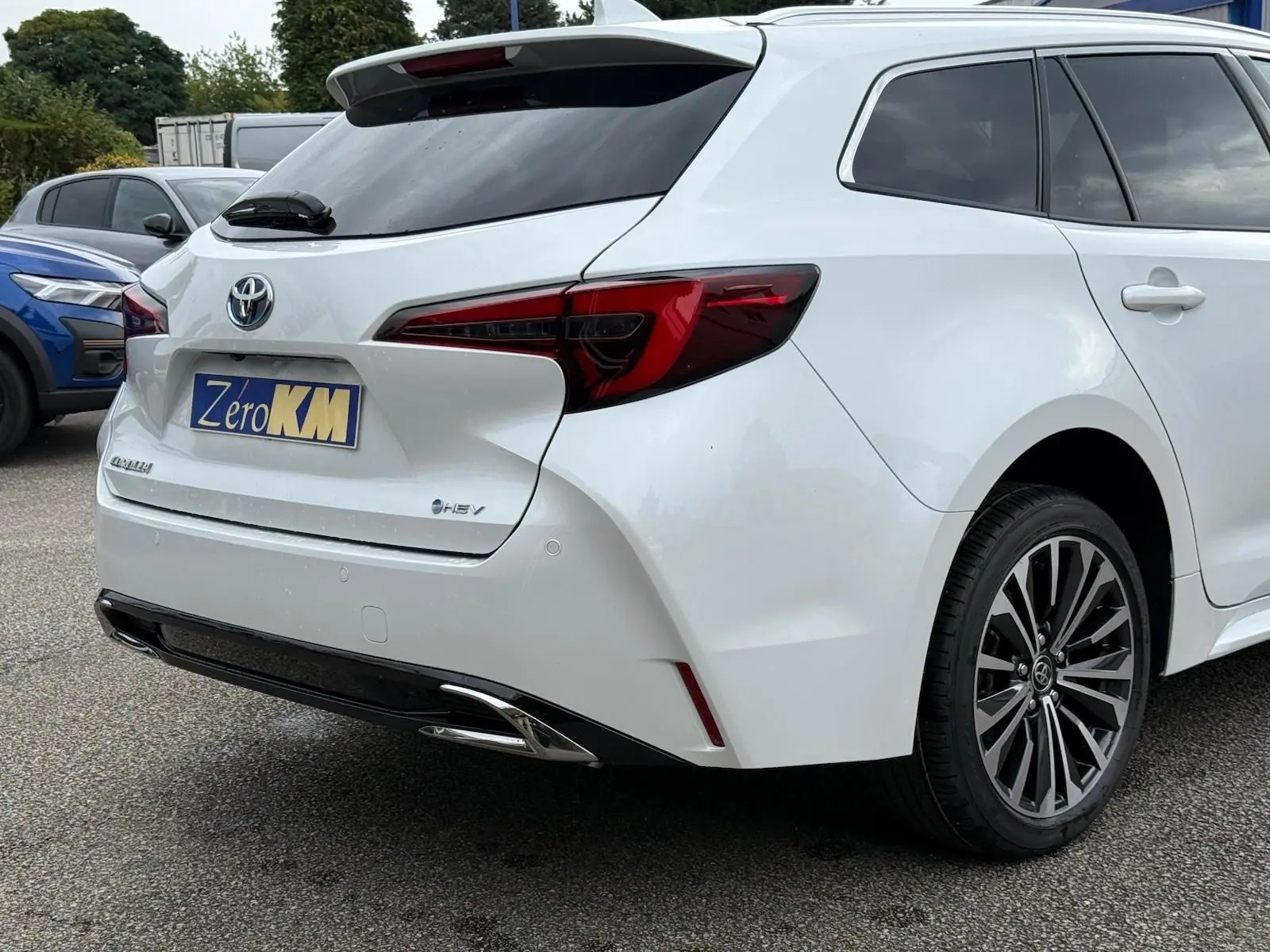 Vue 3/4 arrière droite d'une Toyota Corolla Touring Sport blanche nacrée avec feux arrière LED et jantes alliage noires.