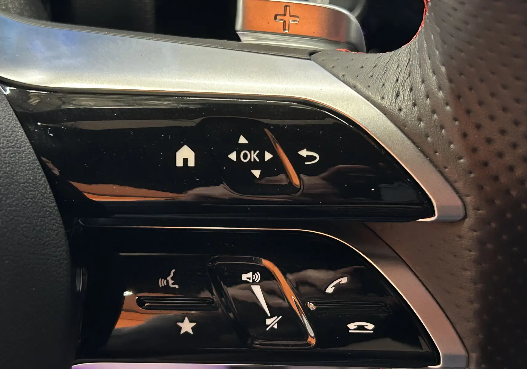 Gros plan sur les commandes noires et argentées du volant perforé côté gauche d'une Mercedes CLA Shooting Brake noire.