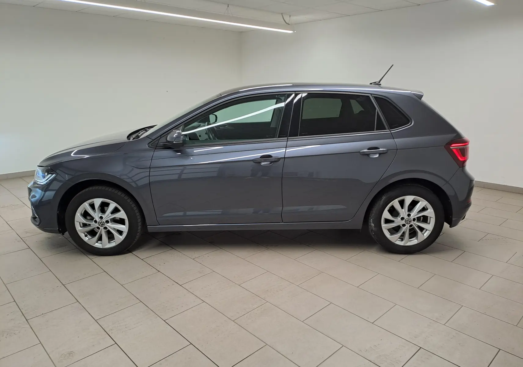 Volkswagen Polo 2023 gris cendré vue de profil côté gauche avec vitres arrière surteintées en intérieur showroom.