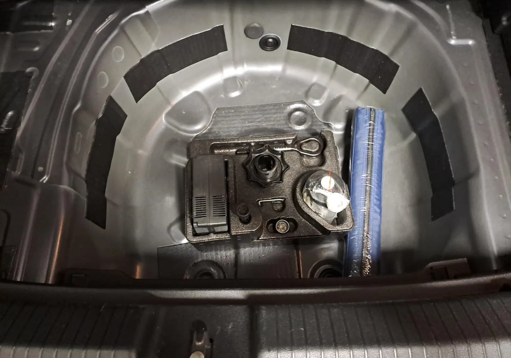 Vue plongeante sur le coffre d'une Volkswagen Polo 2023 gris cendré, montrant le rangement sous le plancher avec outils et kit de réparation.