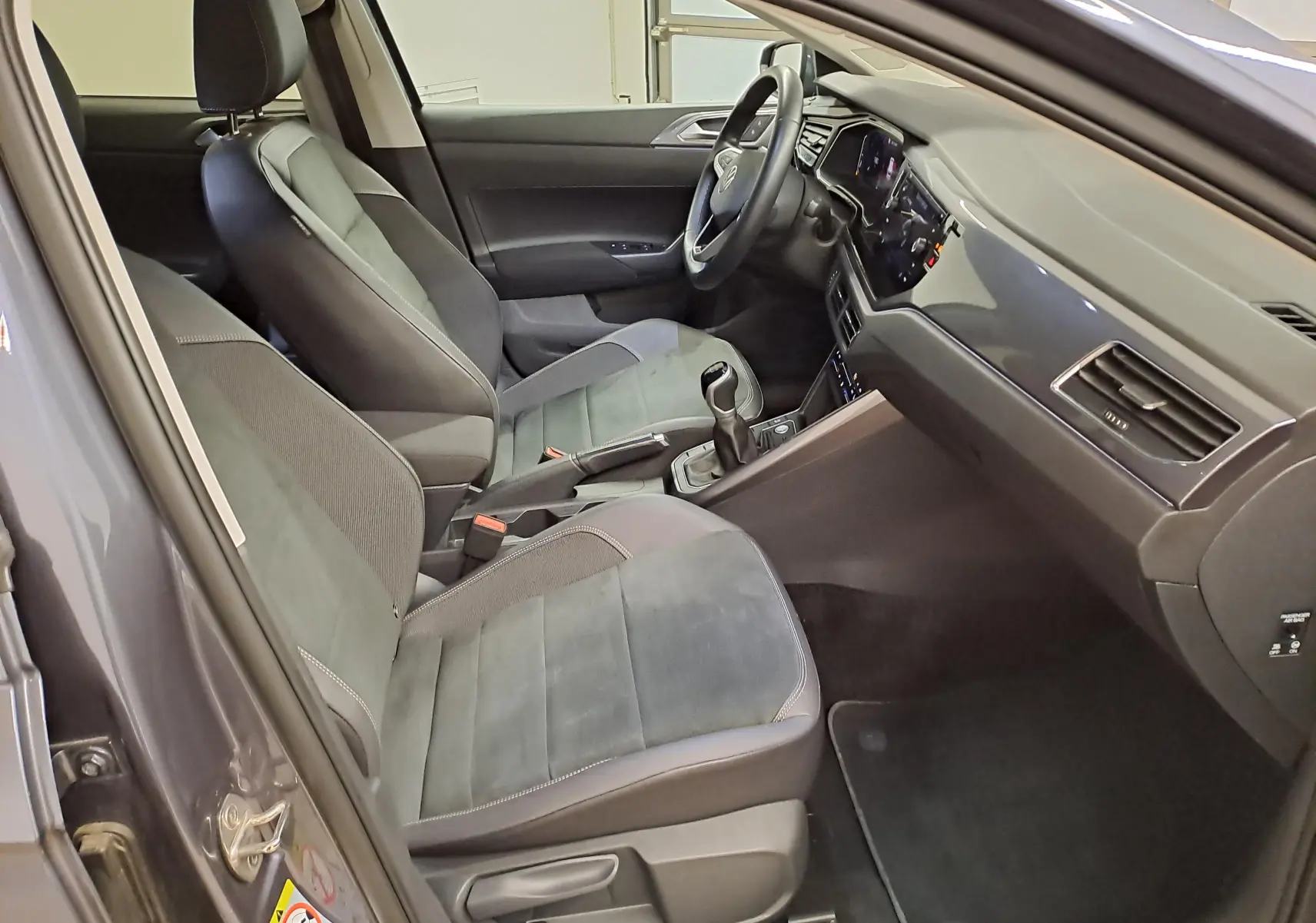 Vue intérieure côté gauche de la Volkswagen Polo 2023, sièges gris, volant multifonction et tableau de bord digital.