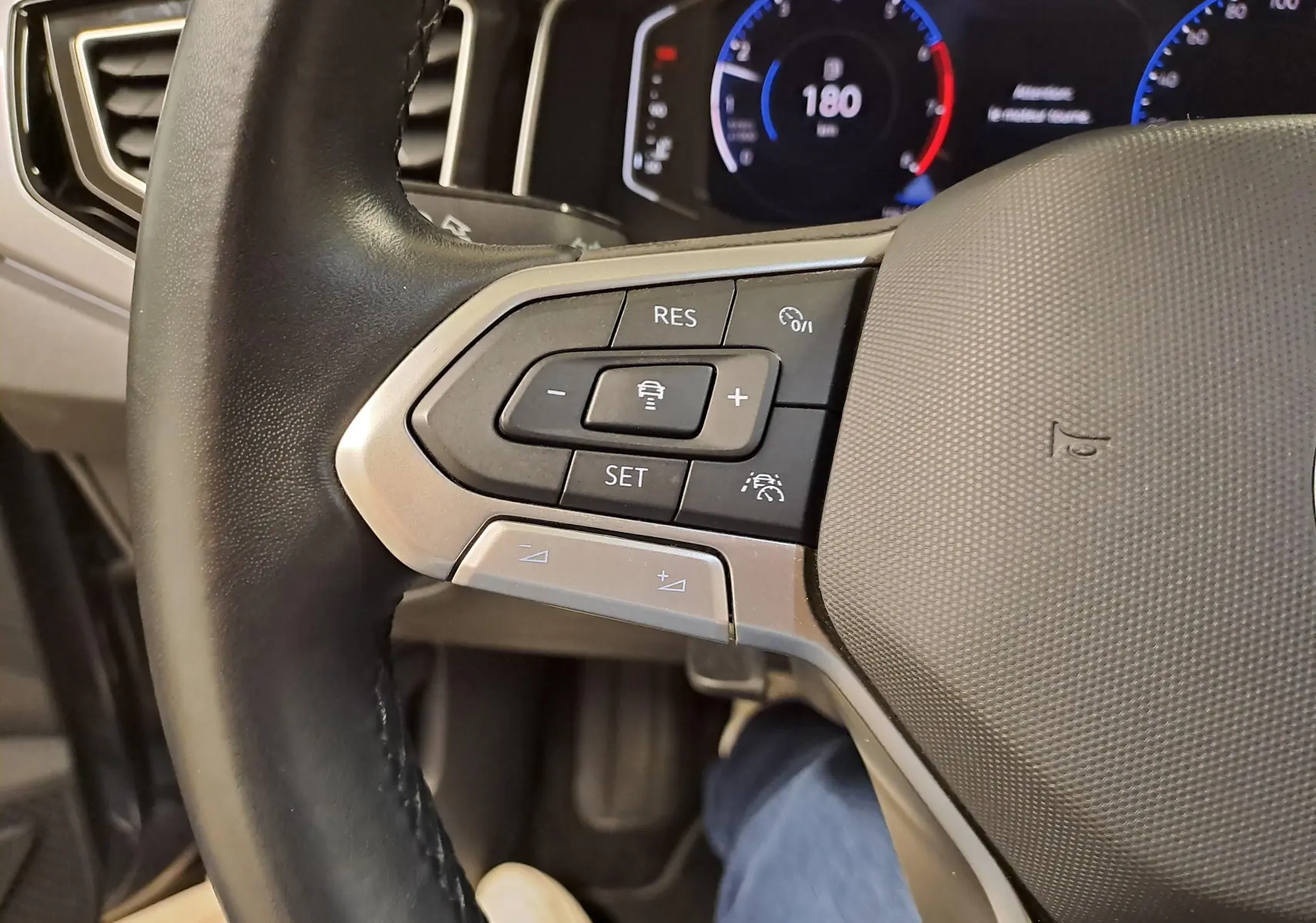 Gros plan sur le volant gauche d'une Volkswagen Polo 2023 avec commandes de régulateur et tableau de bord digital.