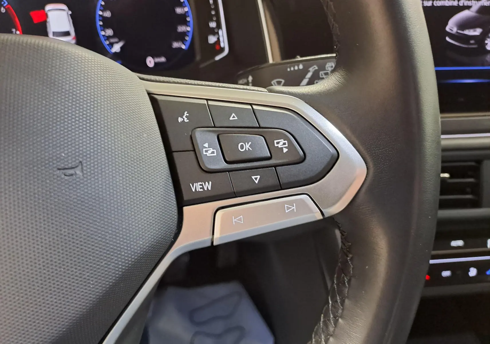 Gros plan sur les commandes au volant cuir noir de la Volkswagen Polo 2023, avec affichage digital en arrière-plan.