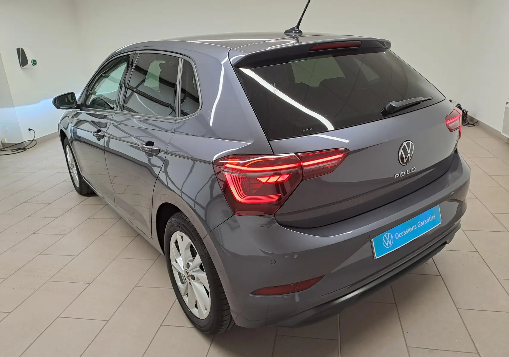Vue 3/4 arrière d'une Volkswagen Polo gris cendré métallisé avec vitres arrière surteintées dans un showroom.