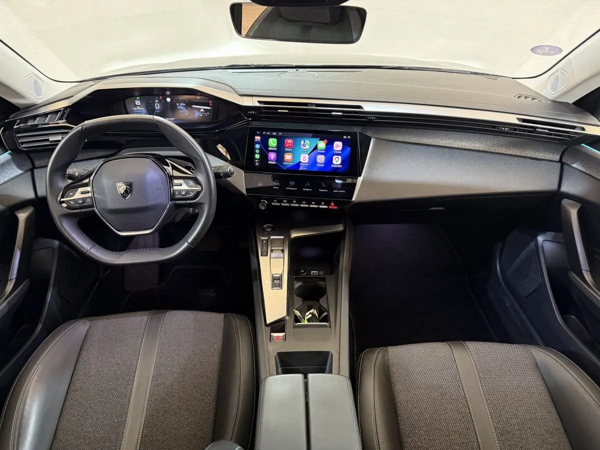 Vue intérieure frontale du tableau de bord et volant cuir noir de la Peugeot 308 SW 2022 avec écran tactile central allumé.