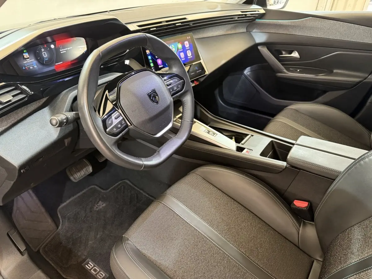 Vue intérieure côté conducteur de la Peugeot 308 gris foncé, avec tableau de bord digital et écran tactile central.