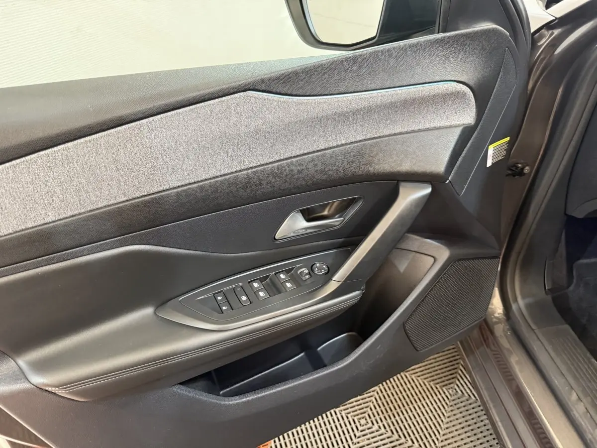 Vue rapprochée de la porte avant gauche de la Peugeot 308 gris foncé, avec commandes électriques et habillage tissu.