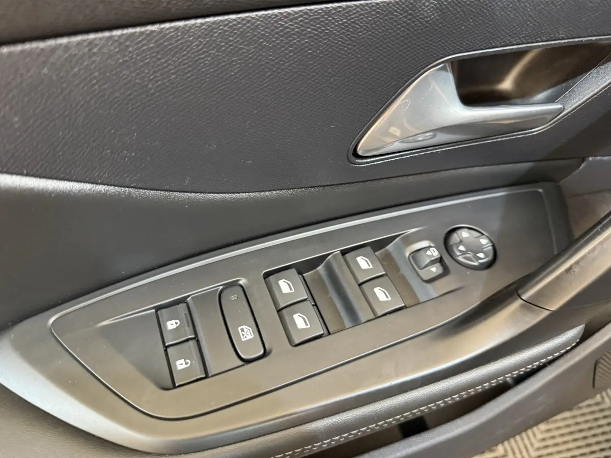 Gros plan sur les commandes des vitres et rétroviseurs côté conducteur de la Peugeot 308 gris foncé, intérieur noir.