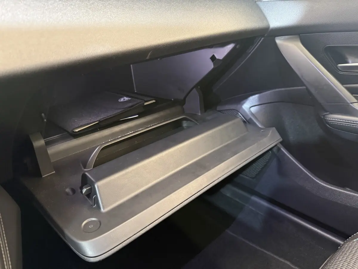 Vue intérieure côté passager de la boîte à gants ouverte de la Peugeot 308 gris foncé, avec rangement et manuel visible.