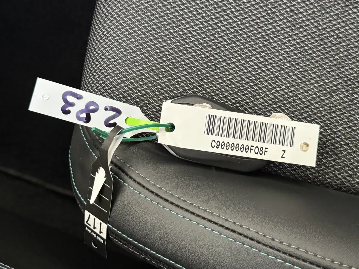 Gros plan sur la clé avec étiquette posée sur un siège tissu gris foncé et cuir noir à surpiqûres bleues du Peugeot 308 SW 2022.