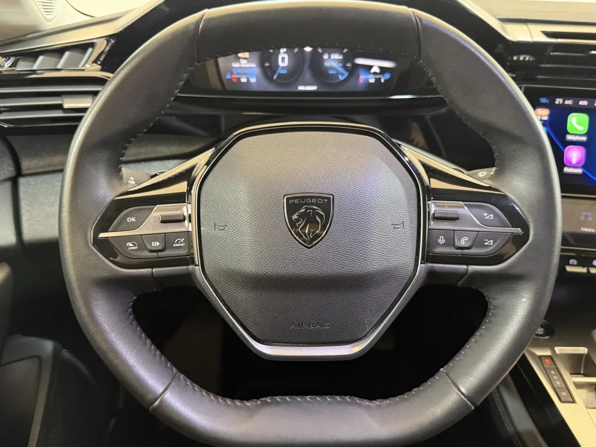 Vue rapprochée du volant cuir noir de la Peugeot 308 2022 avec commandes multifonctions et tableau de bord digital.