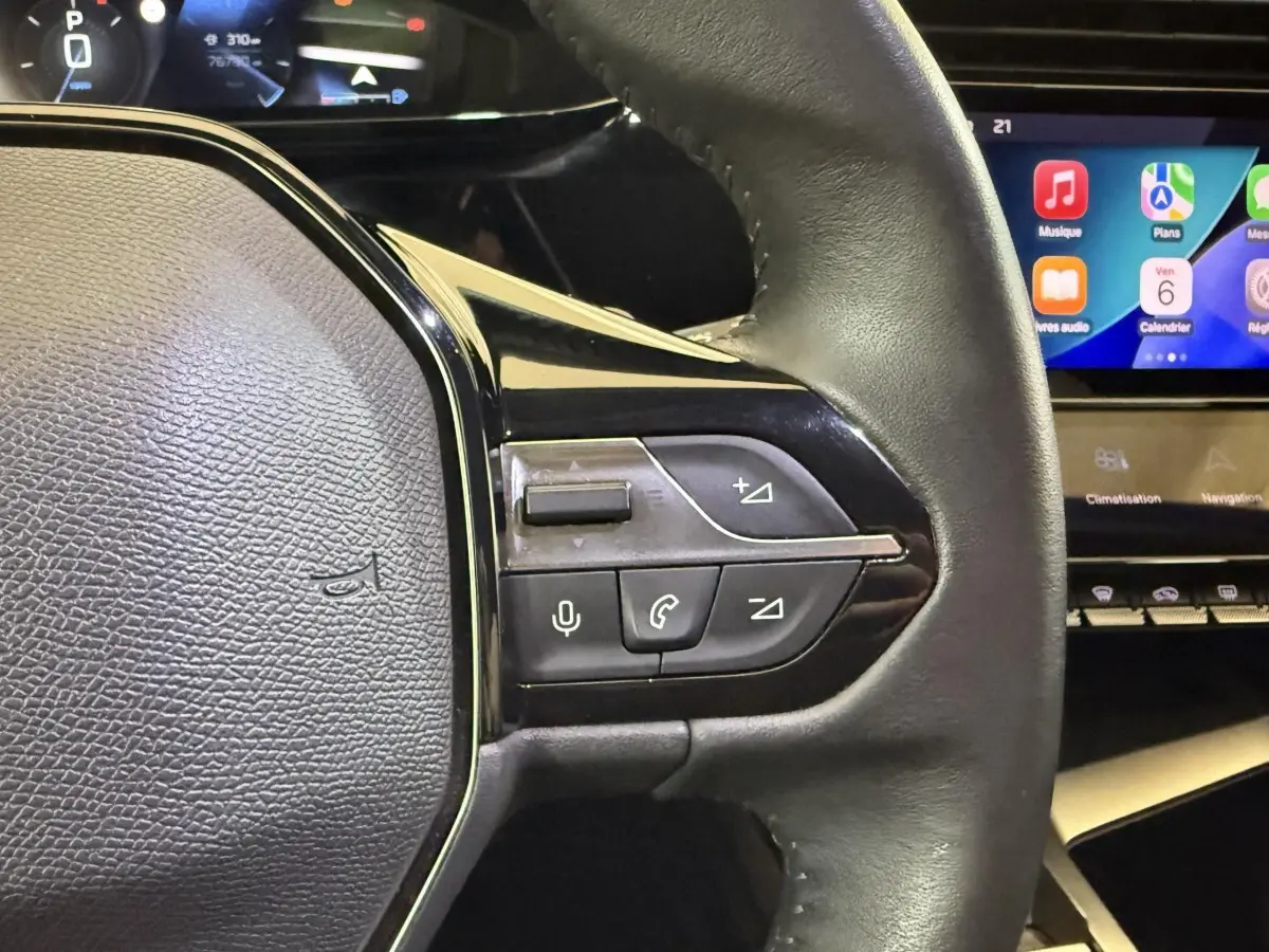Gros plan sur le volant cuir noir de la Peugeot 308 2022 avec commandes vocales et écran tactile en arrière-plan.