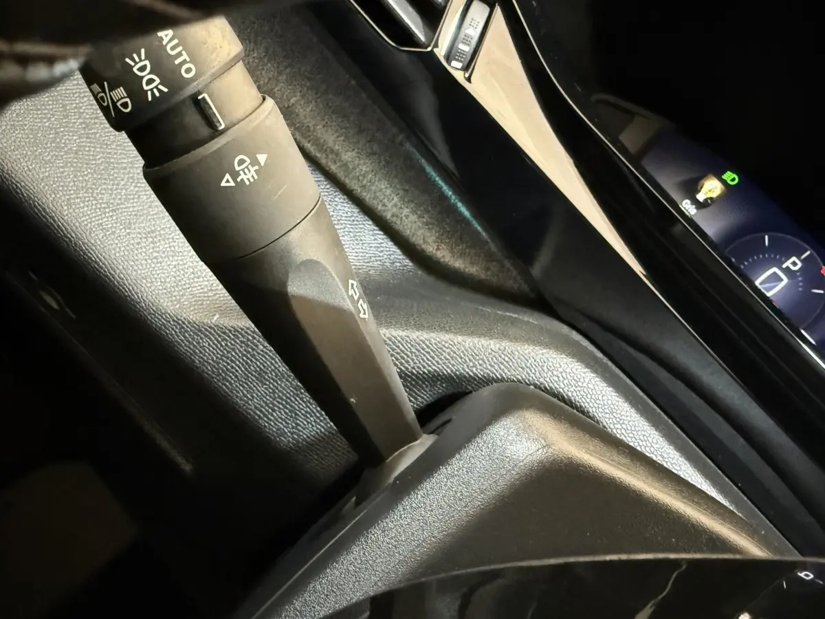 Gros plan sur la commande des feux et le tableau de bord digital bleu de la Peugeot 308 gris foncé, version 2022.