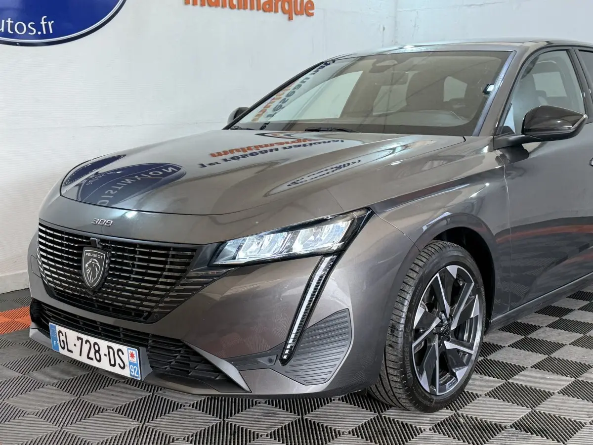 Vue 3/4 avant droit d'une Peugeot 308 SW gris foncé avec calandre noire et feux LED en forme de griffes.