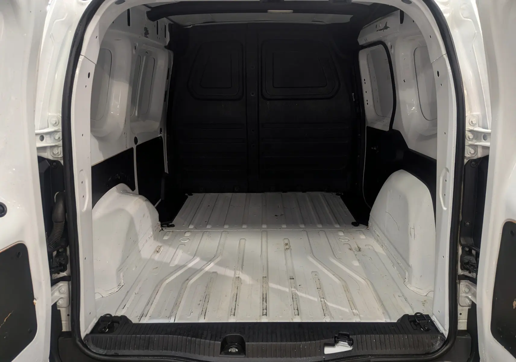 Vue intérieure arrière du Renault Kangoo Van blanc minéral, montrant l'espace de chargement vide et les portes ouvertes.